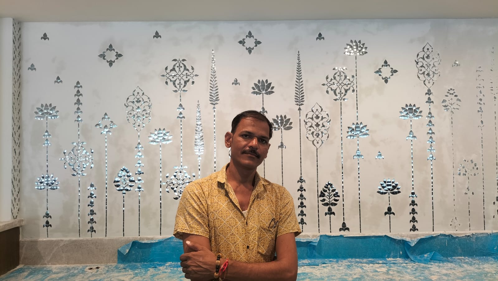 Artist OM standing beside a hand-painted decorative mural in the studio